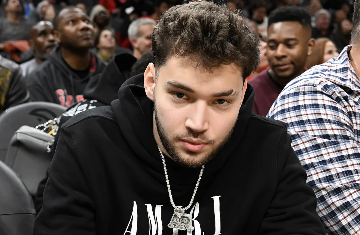 Adin Ross, le Streamer américain assis à un événement arborant une chaîne en diamant de luxe, style lifestyle.