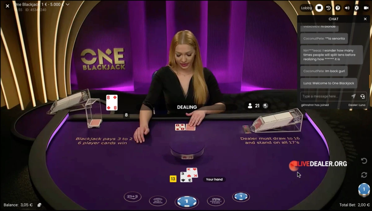 One Blackjack d&eacute;velopp&eacute; par Pragmatic Play, avec une croupi&egrave;re en direct derri&egrave;re une table de blackjack violette, des cartes distribu&eacute;es face visible, l&rsquo;interface de chat en direct, les r&egrave;gles du blackjack affich&eacute;es sur le tapis et le logo One Blackjack en arri&egrave;re-plan.