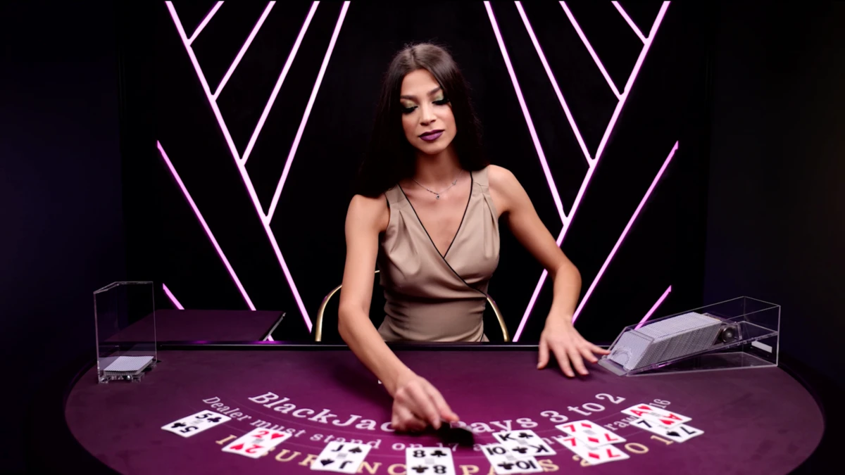 Salon Priv&eacute; Blackjack de l&rsquo;&eacute;diteur Ezugi affichant une croupi&egrave;re en pleine distribution de cartes sur une table de blackjack live violette, avec les r&egrave;gles inscrites sur le tapis, des cartes visibles pour le joueur et le croupier, et un d&eacute;cor studio &eacute;l&eacute;gant aux lumi&egrave;res g&eacute;om&eacute;triques.